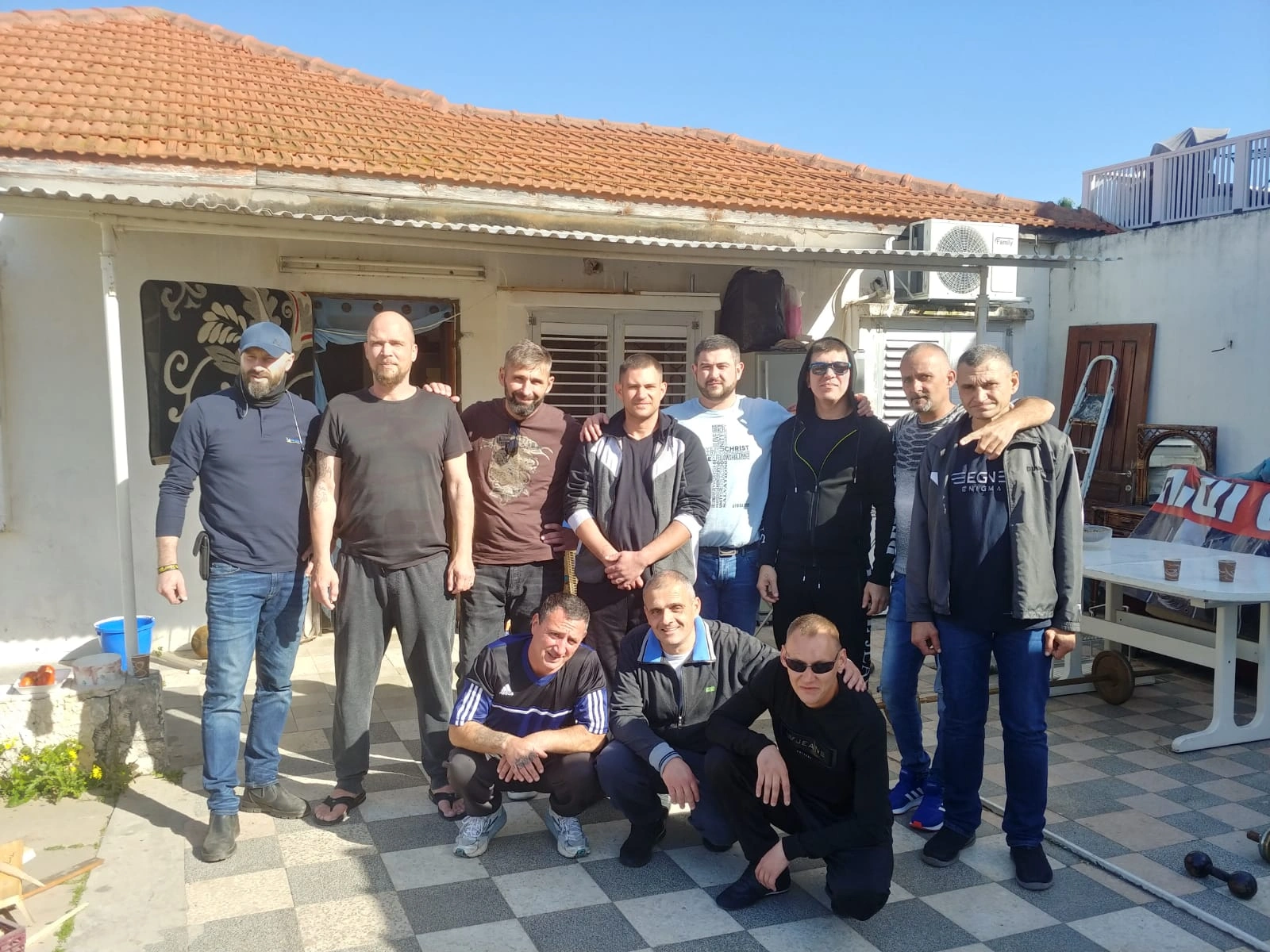 Residents standing and crouching together in the courtyard of the Recovery home.