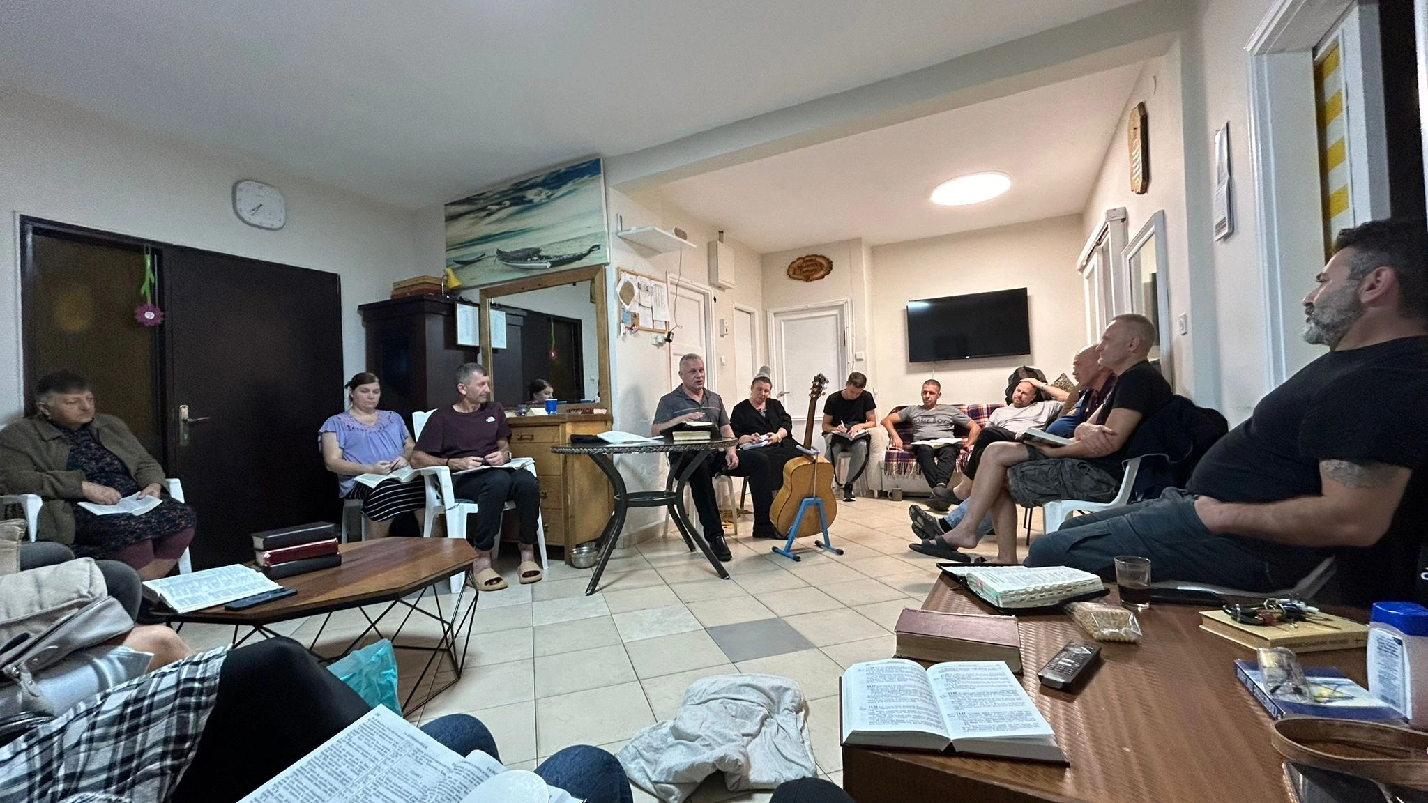 Group of people sitting with open books listening to a leader at the Recovery home.