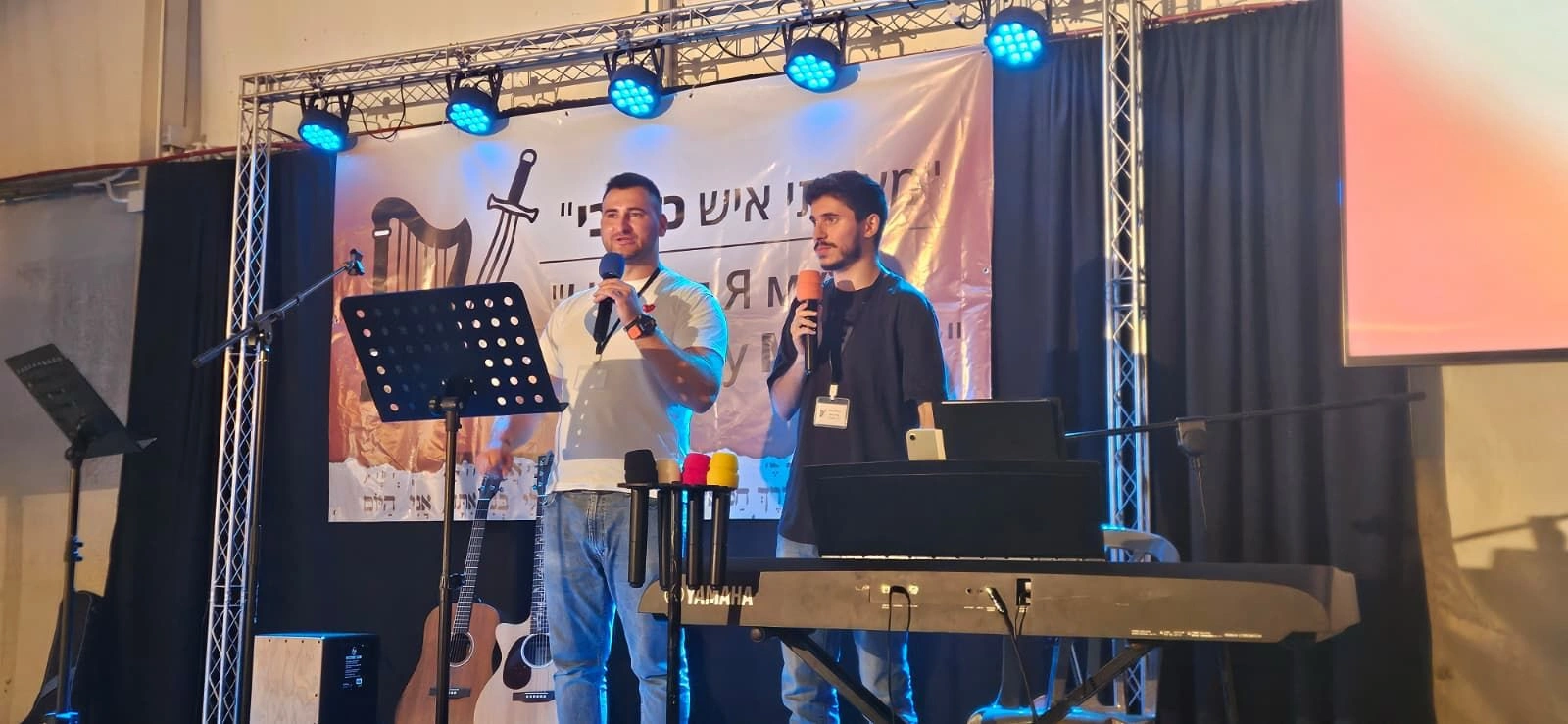 Two men with microphones standing on a stage with blue lighting during the Family conferences.