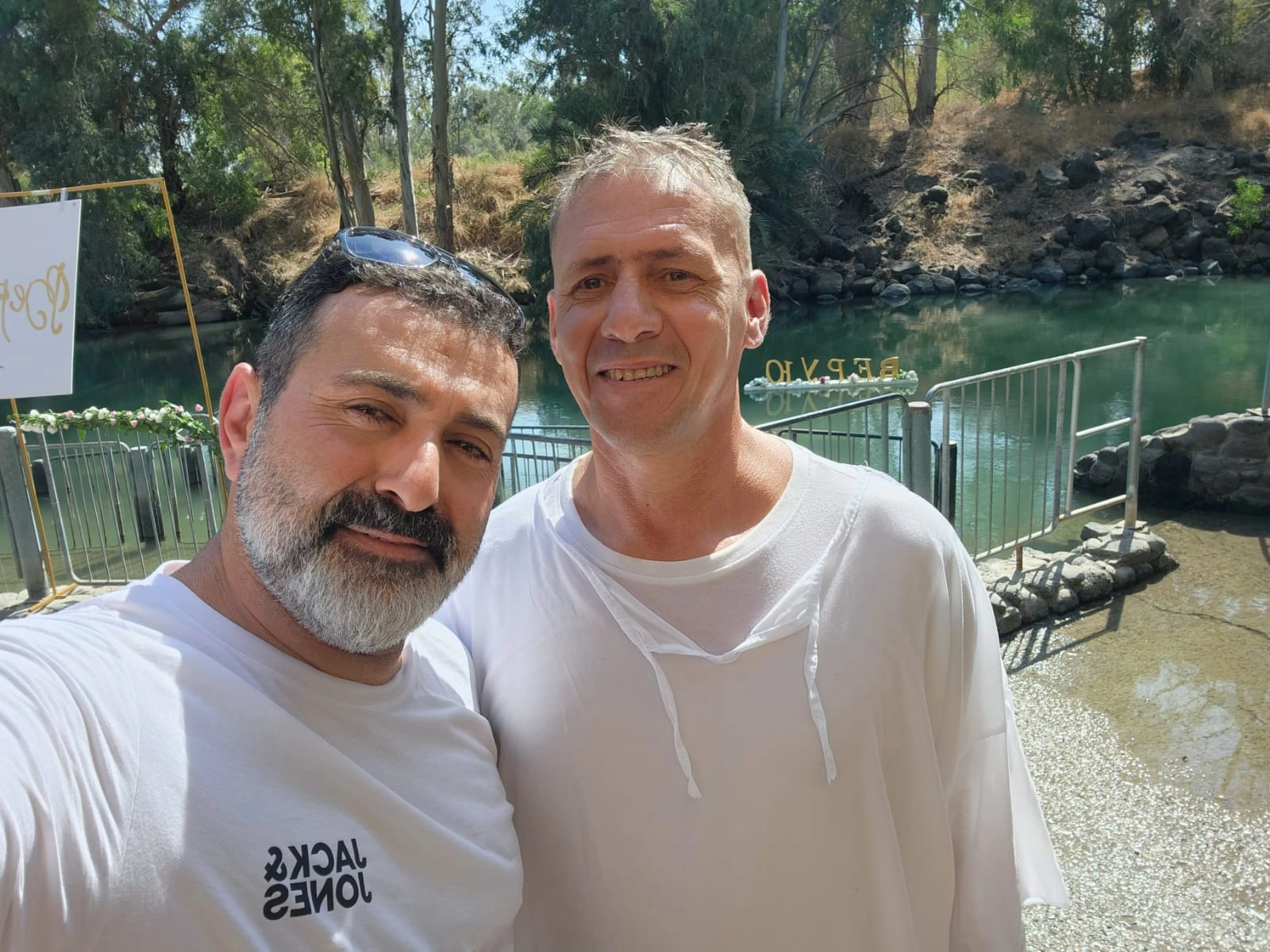 Two men standing arm in arm on a wooden dock near the water at the recovery home.
